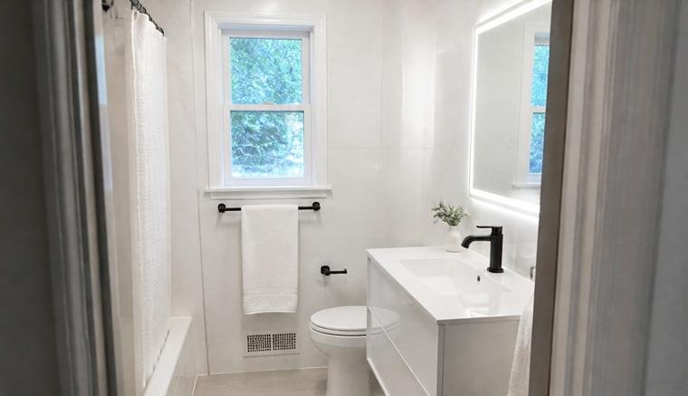 The same bathroom after renovation, finished in white large-format tile with a floating vanity and backlit mirror.