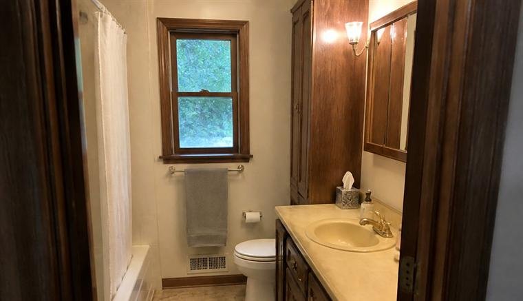 Narrow bathroom with heavy dark wood trim, a brown vanity and a cream sink, before renovation.