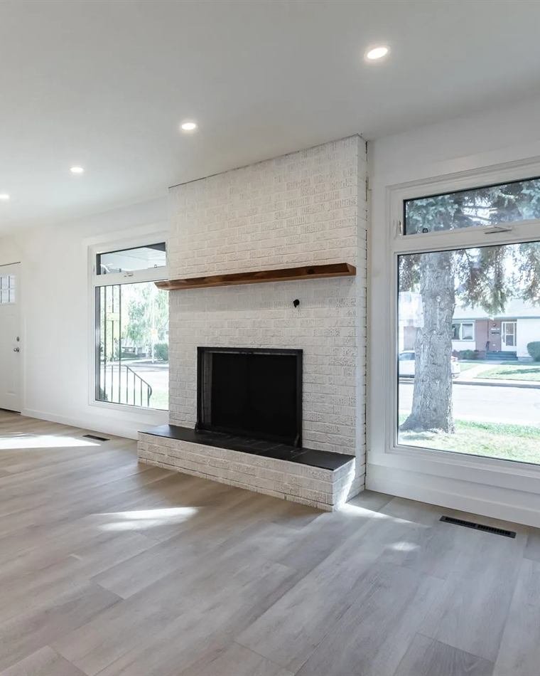 A finished living room with a whitewashed brick fireplace, timber mantel and new plank flooring.